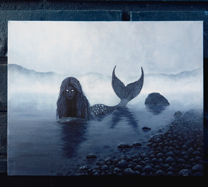 Mermaid with dark hair and tail emerging from water on a foggy night.