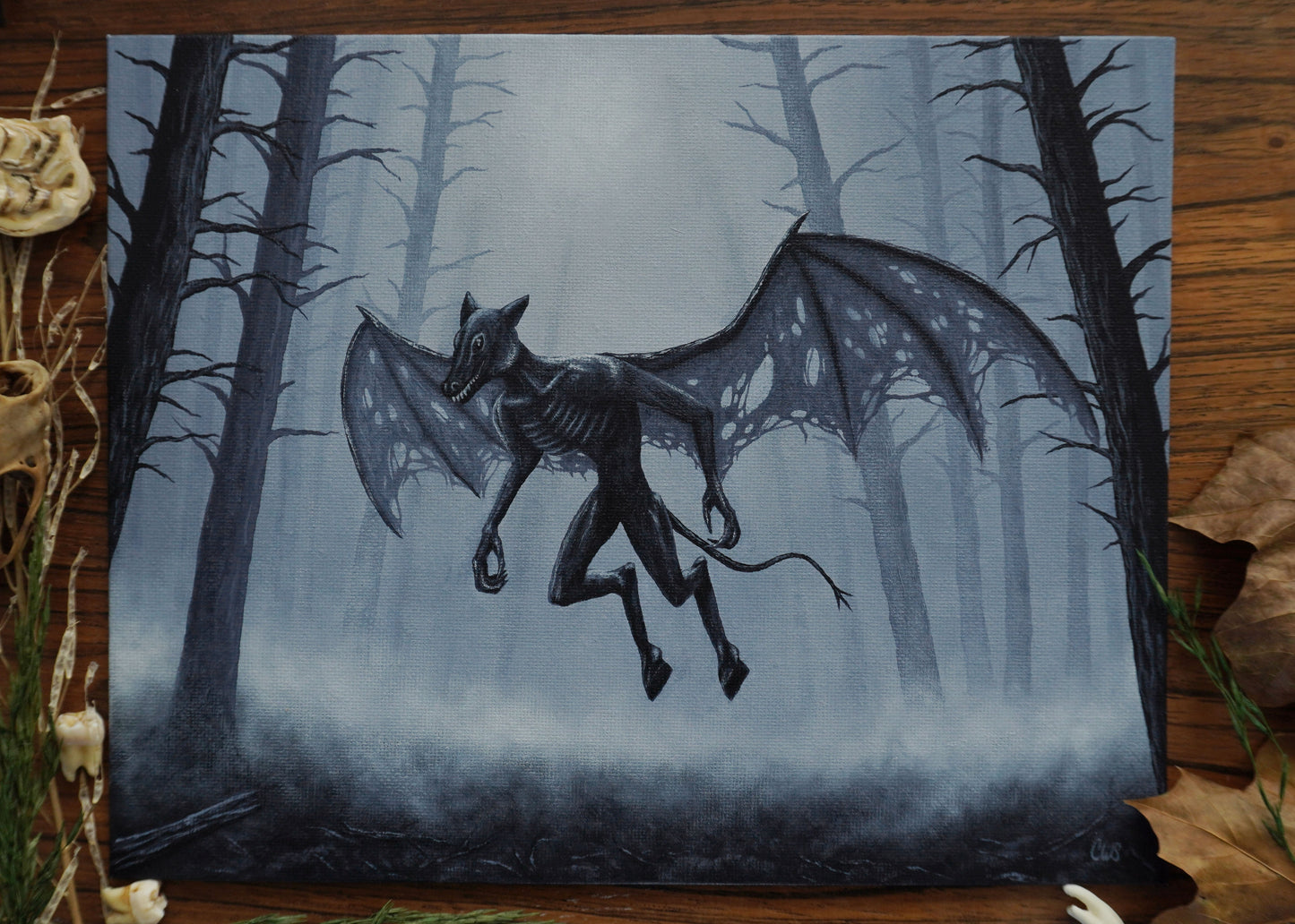 Painting of a winged creature in a forest on a wooden surface with natural elements.