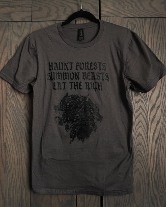 Dark gray t-shirt with graphic design and text, it features cerberus and the words haunt forests summon beasts eat the rich