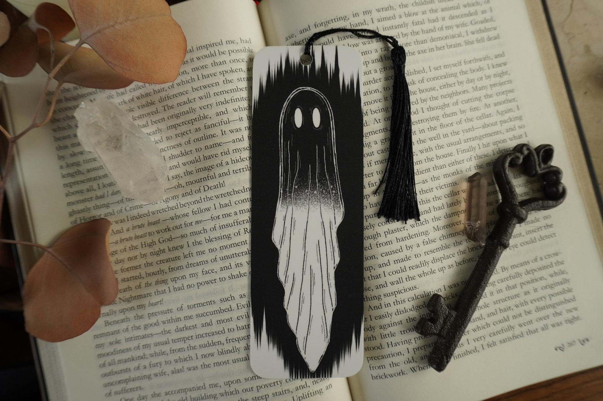 black and white Ghost bookmark  with a.black tassel on an open book with a key and dried leaves.