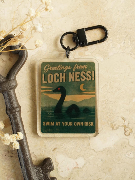 Keychain with 'Greetings from Loch Ness! Swim at your own risk' design on a textured background