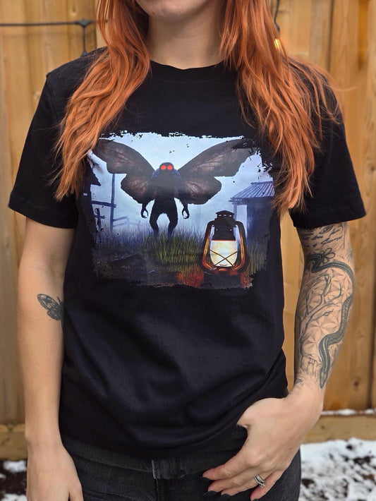 Person wearing a black t-shirt with a graphic design of a mothman with glowing red eyes