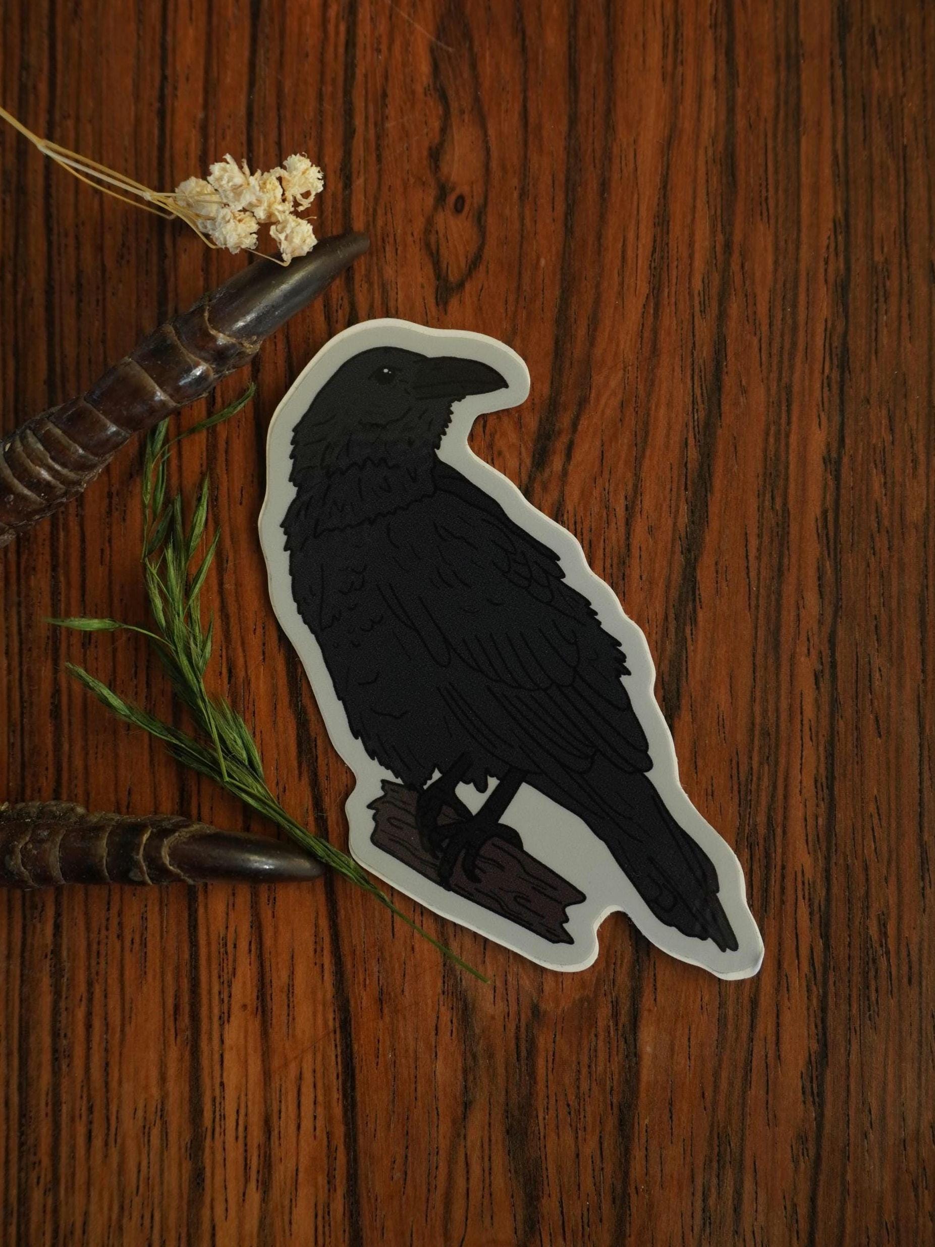 Sticker of a raven on a wooden surface with dried flowers and branches.