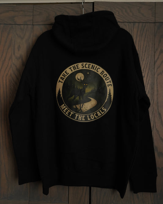 Black hoodie with a circular logo that says take the scenic route meet the locals, it has a campy vibe